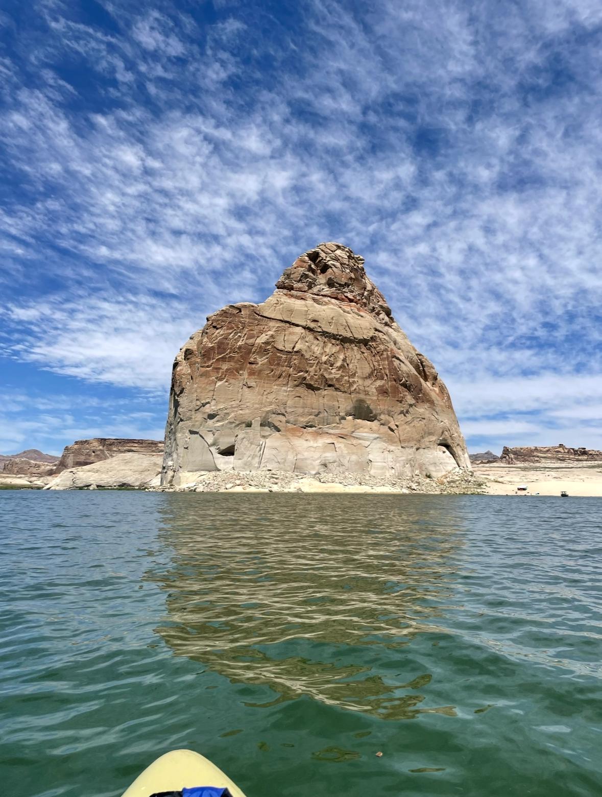 Lone Rock, a tall sandstone butte, rising from green-blue water in front of the nose of the paddle board.